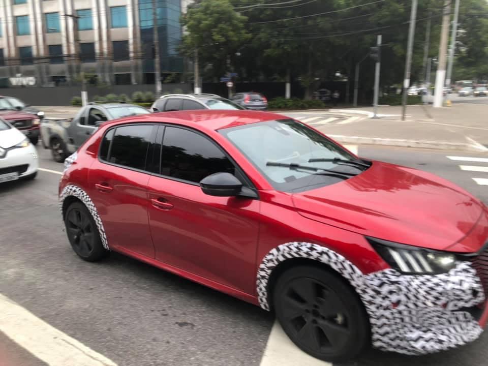 Peugeot 208 vermelho rodando na cidade de São Paulo com adesivos nos para-lamas e no para-choques e com os faróis com três barras verticais de leds