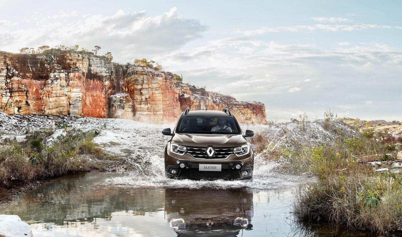 Novo Renault Duster de frente atravessando pequeno trecho de ágia em meio a uma estrada de pedra e ao fundo um grande cânion alaranjado