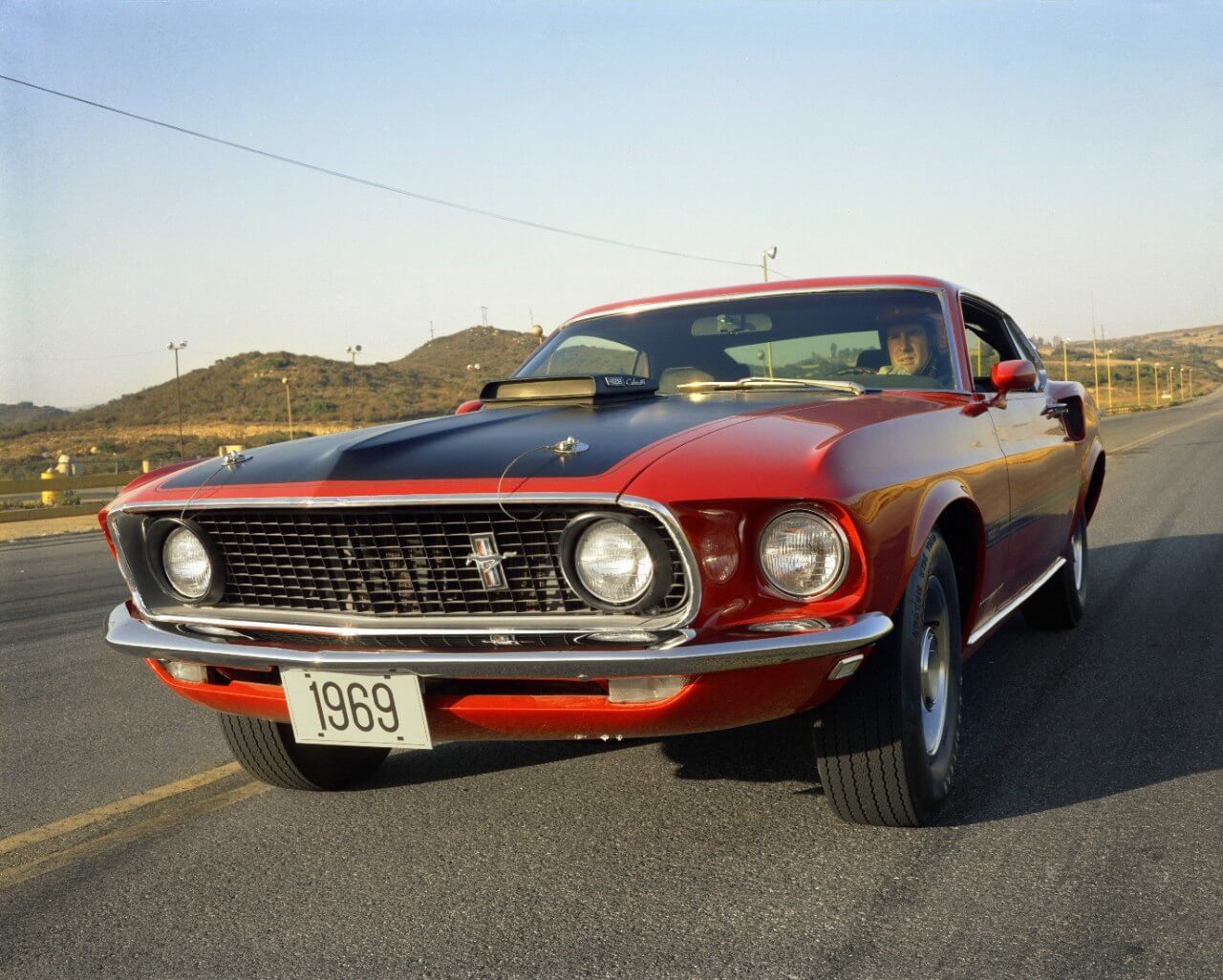 Ford Mustang Mach 1 1969 vermelho com faixa preta sobre o capô e entradas de ar e faróis auxiliares redondos na grade