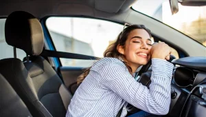 Jovem feliz após escolher o primeiro carro no Feirão e Black Feirão Webmotors e fazer a compra abraçando o volante